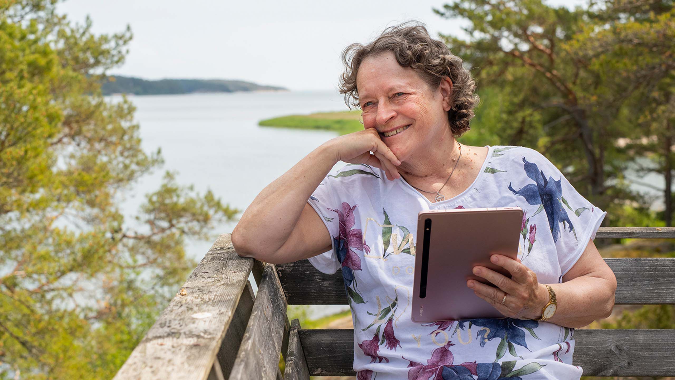 Rouva istuu ulkona penkill&auml; tabletti k&auml;dess&auml;&auml;n